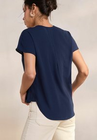 Top blu navy a maniche corte con una vestibilità rilassata, caratterizzato da un orlo arrotondato e aperture laterali. Abbinato a jeans chiari.