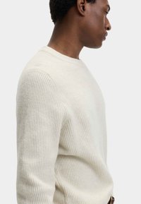 Cremfarbener gerippter Pullover mit Rundhalsausschnitt und langen Ärmeln, der ein strukturiertes Strickmuster und einen lässigen Schnitt aufweist.