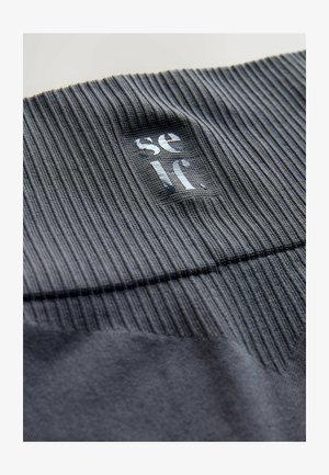 Szare prążkowane tkaniny z gładkim panelem ozdobionym odblaskowym logo marki. Materiał ma miękką teksturę z różnorodnymi wzorami dzianiny.