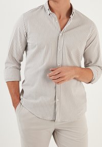 Camicia a righe beige e bianca, con maniche lunghe e polsini arrotolati, colletto classico e tessuto testurizzato.