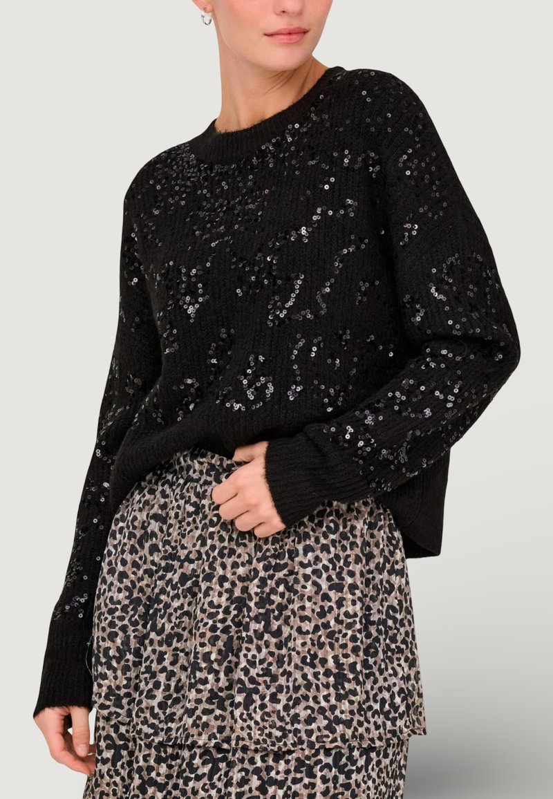 Pull en tricot noir orné de sequins brillants, avec des manches longues et un col rond, associé à une jupe beige à imprimé léopard.
