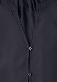 Gros plan sur le devant d'une chemise en tissu sombre avec deux petits boutons et des coutures visibles le long des coutures.