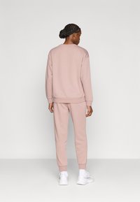 Ανοιχτό ροζ φούτερ και ταίριαστο παντελόνι φόρμας από απαλό ύφασμα. Διαθέτει ριμπ μανσέτες και μέση. Το σύνολο ολοκληρώνουν λευκά αθλητικά παπούτσια.