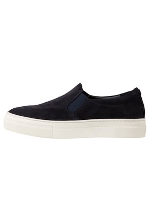 Zapatos de ante azul marino tipo slip-on con paneles elásticos en los lados y suela de goma blanca. Presentan una textura suave y un diseño de punta redondeada.