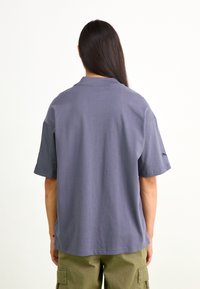 Camisa polo de manga corta gris con cuello estándar y corte relajado, hecha de material de algodón suave. Presenta un diseño simple con acentos mínimos.