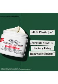 Kiehl's Ultra Facial Cream i en hvit plastkrukke med et lokk, som inneholder en kremfarget produkt og rød tekst på en grønn bakgrunn.
