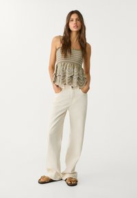 Ljus olivfärgad peplumtop med broderad scalloped fåll, kombinerad med krämfärgade vida byxor. Klädseln kompletteras av bruna sandaler.