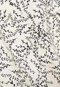 Tissu blanc avec un motif de vigne feuillue noire, présentant une couture et de légers plis pour ajouter texture et profondeur.
