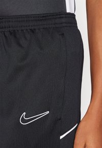 Nike svarte treningsshorts med en myk tekstur, elastisk midjebånd, hvit logo-broderi og sidelommer. Ingen distinkte mønstre eller aksenter.