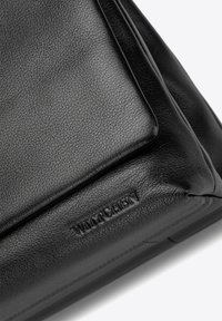 Sac en cuir noir avec une finition texturée, de forme carrée et avec un logo en relief. Présente des lignes épurées et un design minimaliste.