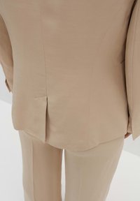 Completo beige su misura con finitura testurizzata, spacco singolo sul retro e silhouette strutturata in tessuto morbido.