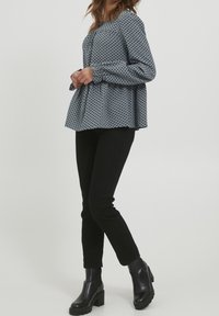 Blusa blu a pois con design svasato e maniche lunghe, abbinata a pantaloni neri attillati e stivali neri con tacco chunky.