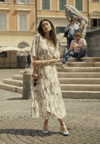 Hosszú, bézs színű ruha lómintával, fodros szegéllyel, világoskék lapos cipővel párosítva. A helyszín macskaköves utcákból áll.