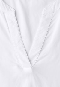 Tissu blanc avec un col en V présentant de larges revers cousus, montrant la texture et les coutures sur un fond lisse et uni.