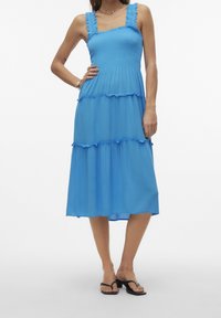 Robe bleu à volants avec un corsage ajusté, des bretelles froncées et une jupe fluide. Tissu léger avec une texture lisse et longueur mi-mollet.