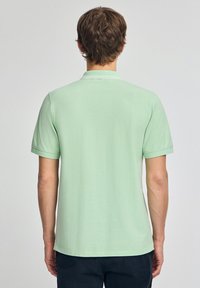Jasnozielona koszulka polo z krótkim rękawem o gładkiej fakturze, z klasycznym kołnierzykiem i prostym dołem, prezentowana od tyłu.