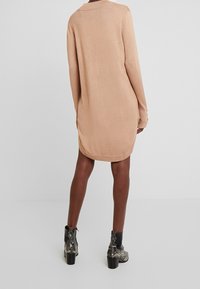 Abito maglione a maniche lunghe in beige chiaro. Presenta un collo rotondo, un orlo leggermente curvo ed è abbinato a stivali alla caviglia con stampa serpente nera.
