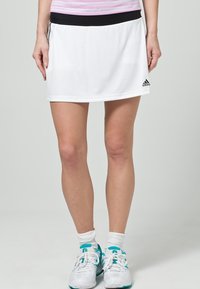 Falda de tenis blanca con cinturilla negra, hecha de una tela ligera. Presenta un logo de Adidas en el lado izquierdo y una textura suave.