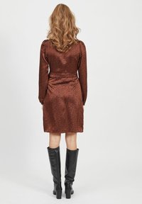 Vestido de satén marrón con estampado de animal negro, mangas largas, cintura ceñida y dobladillo a la altura de la rodilla, combinado con botas negras hasta la rodilla.