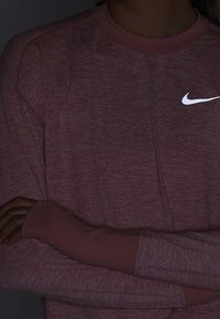 Rotes meliertes Langarm-Sportshirt mit geripptem Rundhalsausschnitt und Bündchen. Mit reflektierendem weißen Nike-Logo auf der Brust. Glatte Textur.