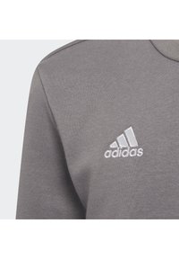 Grå hettegenser med teksturert stoff, rund hals og en hvit brodert Adidas-logo på øvre venstre brystområde.