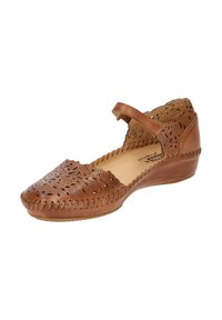 Chaussure en cuir marron avec un motif floral perforé, bout rond et une brides à la cheville. Elle présente un talon compensé bas et des bords cousus.