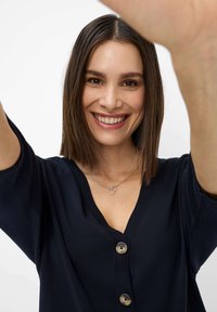 Top in maglia blu navy a maniche corte con scollo a V e tre grandi bottoni. Due anelli d'argento intrecciati su una delicata collana.