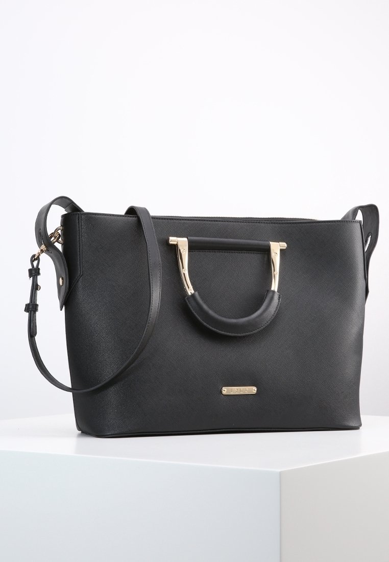 Svart syntetläderhandväska med guldfärgade detaljer, dubbla handtag och avtagbar axelrem. Har en strukturerad form och texturerad yta.