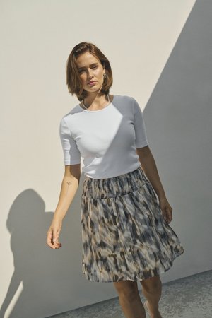 T-shirt blanc ajusté à manches courtes associé à une jupe plissée de longueur genoux avec des motifs abstraits en marron, gris et crème.