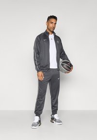 Gray athletic tracksuit with white stripes and Nike logos, paired with a white t-shirt and black and white sneakers, holding a basketball.