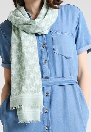 Écharpe vert clair à motifs d'étoiles enroulée autour du cou sur une robe en jean bleu à manches courtes avec boutons, ceinture à la taille et poche poitrine.