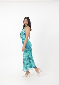Un lungo vestito fluente nelle tonalità di blu e verde con un motivo floreale, con collo all'americana e dettagli coordinati con nastri. Abbinato a tacchi di colore chiaro.