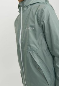 Giacca leggera verde menta realizzata in tessuto liscio, con cerniera frontale completa, cappuccio e logo sul petto.