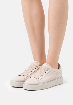 Beige mokkasiner i semsket skinn med rund tå, flate lisser og en teksturert gummisåle. Minimalistisk design med glatte overflater og subtile detaljer.