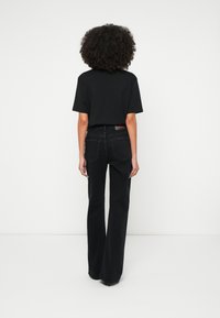 Tricou negru cu mâneci scurte, asortat cu blugi negri evazați. Blugii au un design standard pentru buzunarul din spate și un etichetă colorată pe talie.