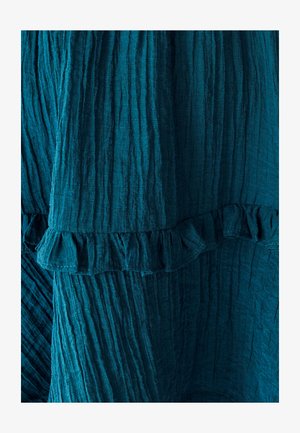 Teal textiel met een gestructureerd oppervlak, voorzien van verticale plooien en een ruffled zoom. Zacht, valt soepel en benadrukt diepte en beweging in het ontwerp.