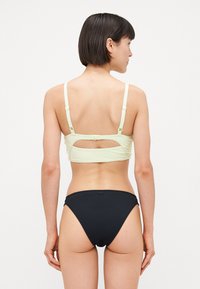 Haut de bikini vert clair avec des bretelles réglables et un dos découpé, accompagné d'un bas de bikini noir, présentant un design simple et une texture lisse.