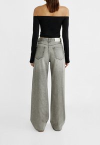 Czarny top na ramiączkach z długim rękawem zestawiony z szarymi spodniami typu wide-leg; spodnie mają tylne kieszenie i lekko przyblakłą strukturę.