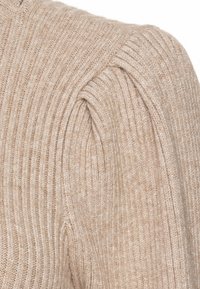 Beige ribbestrikket genser med puffede skulderdetaljer, som viser en myk tekstur og avslappet passform. Synlig søm gir designinteresse.