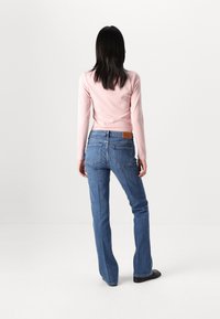 Ljust rosa ribbad långärmad topp i kombination med blå bootcut-jeans med bakfickor och en beige läderlapp på gördeln.
