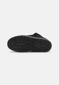 Zapato deportivo negro con una suela de goma texturizada que presenta un patrón de surcos y crestas para mejorar el agarre. Diseño simple y funcional.