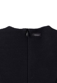 Černý top z žíhané tkaniny s uzavíráním na zip vzadu a malou nálepkou, který předvádí strukturovaný povrch a minimalistický design.