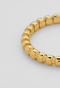 Goldfarbener elastischer Armreif, bestehend aus runden Perlen mit einer glatten, glänzenden Oberfläche, die ein einheitliches Design und eine nahtlose Textur aufweisen.