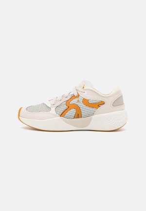 Baskets beige clair avec semelle blanche, accents orange, motif à quadrillage noir et lacets, vues de côté sur un fond uni.