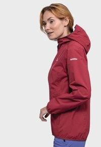 Red waterproof jacket with a hood, featuring elastic cuffs, a zippered front, and a logo on the sleeve. Smooth texture and lightweight design.