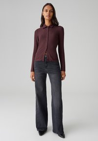 T-shirt long à rayures bordeaux avec un col, fermeture à boutons à l'avant, associé à un jean noir à taille haute et jambes larges.