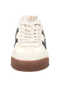 Béžové semišové tenisky s černými akcenty a hnědou gumovou podrážkou. Mají texturované tkaničky a výrazné logo na jazyku.