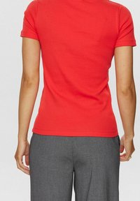 T-shirt en coton rouge à manches courtes, design ajusté et col rond. Associé à un pantalon gris à rayures fines présentant une coupe droite.