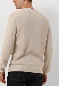Maglione beige con un design a maglia testurizzata, collo rotondo e un sottile accentuazione a strisce sul retro. Abbinato a jeans scuri.