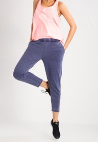 Top in cotone rosa realizzato in un tessuto leggero, abbinato a pantaloni jogger blu con una vestibilità comoda e cintura elastica. Scarpe da ginnastica nere.